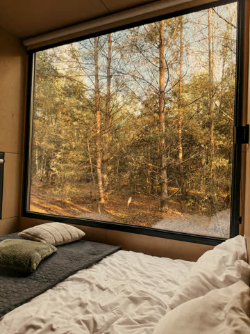 Cabin bedroom with a picture window onto a golden pine forest